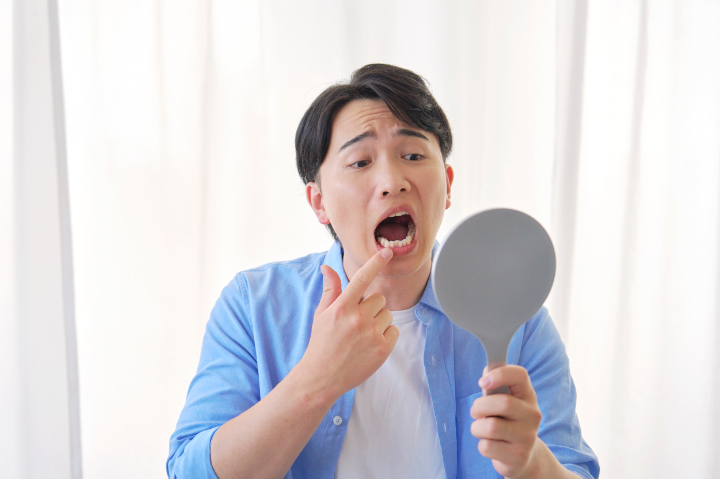 割れたセラミックの歯を鏡で確認している男性